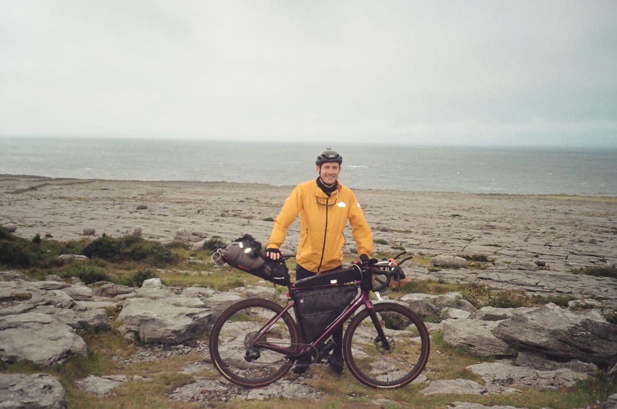 A bikepacker standing with a loaded touring bike on a rocky coast