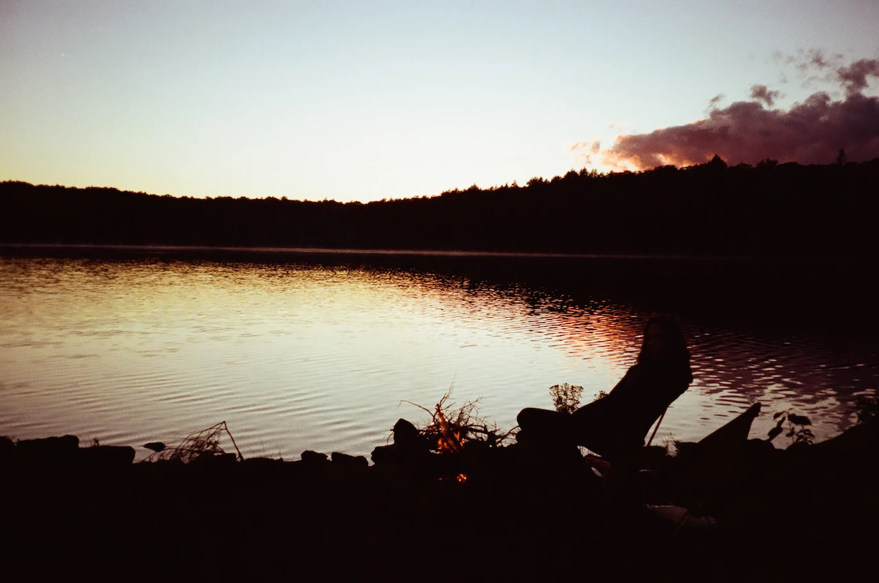 A dark shoreline reflected in still water after sunset