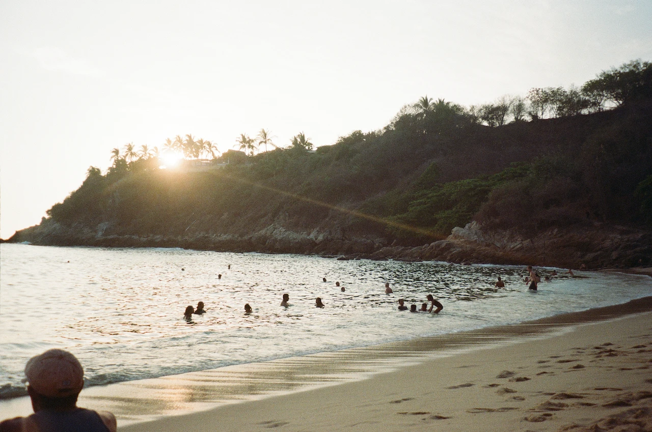 Distant swimmers gathered in a sheltered bay as the sun reaches the headland