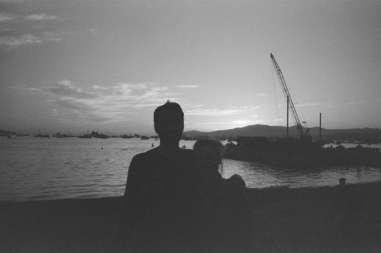 An anonymous silhouette facing a working harbour at sunset