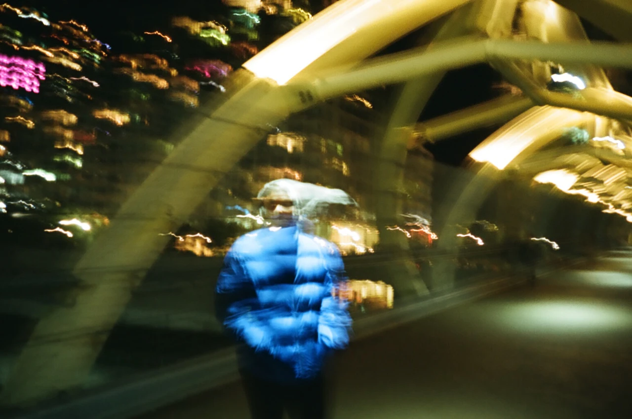 A blue figure and city lights dissolved into streaks by camera movement