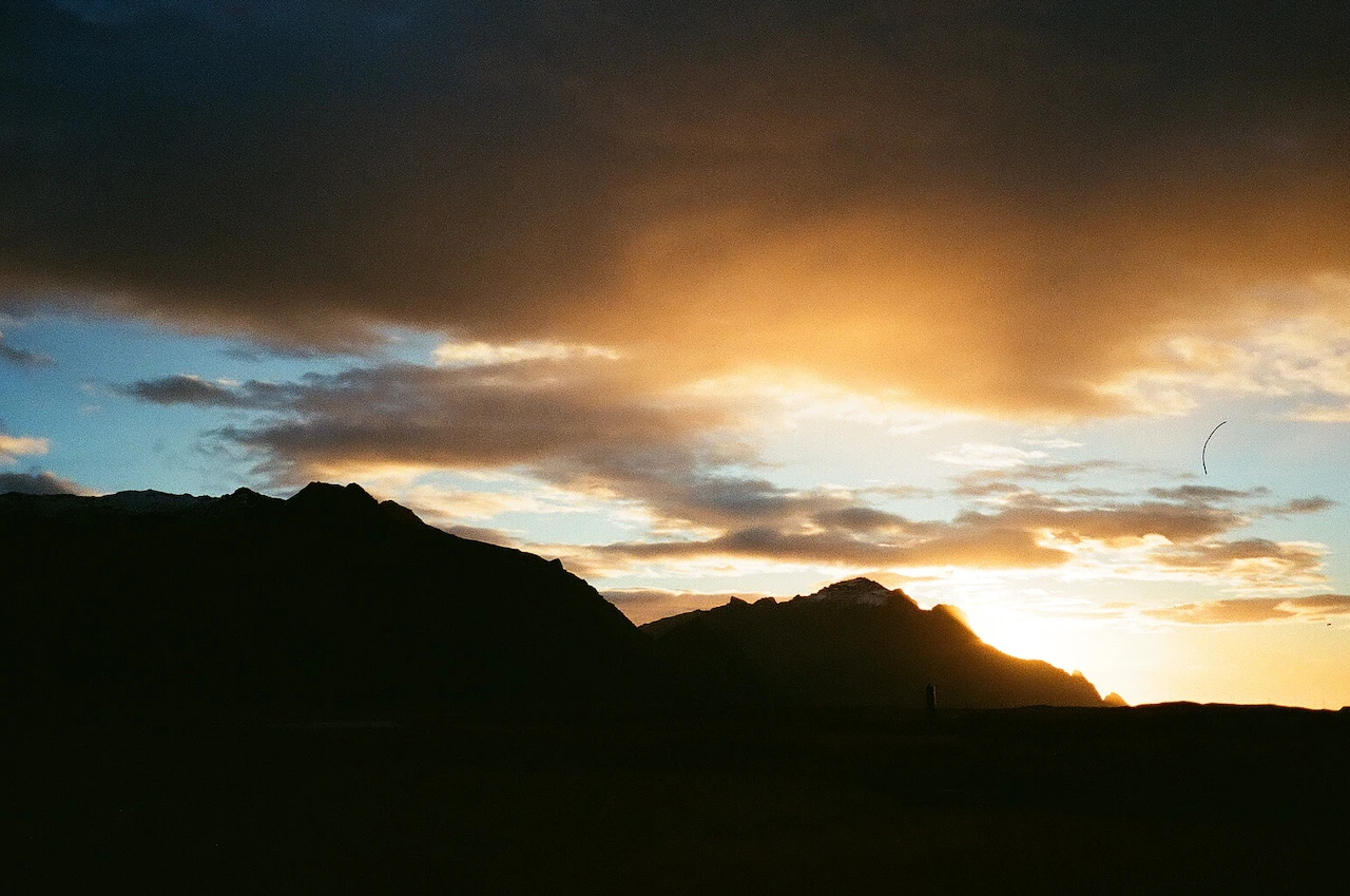Golden light breaking beneath dark storm clouds behind a jagged ridge
