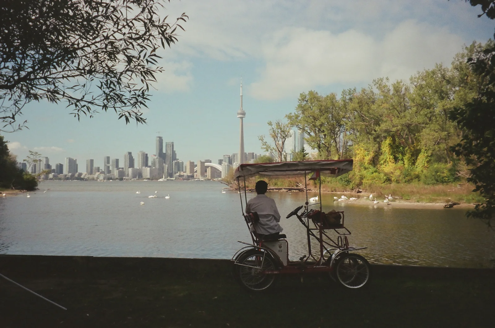 A cyclist beside a loaded bicycle on a waterfront with a distant city skyline