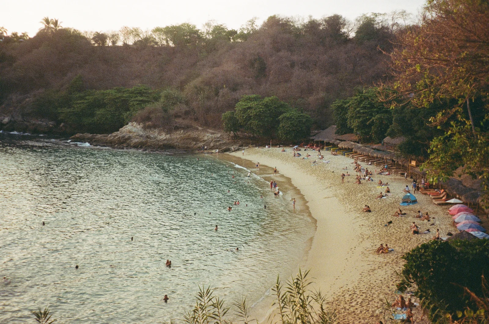 A busy sheltered beach curving around a clear green cove