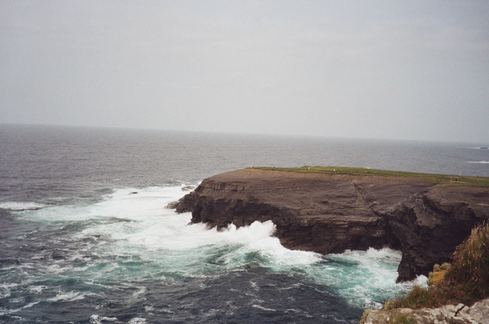 A low grassy headland surrounded by white Atlantic surf