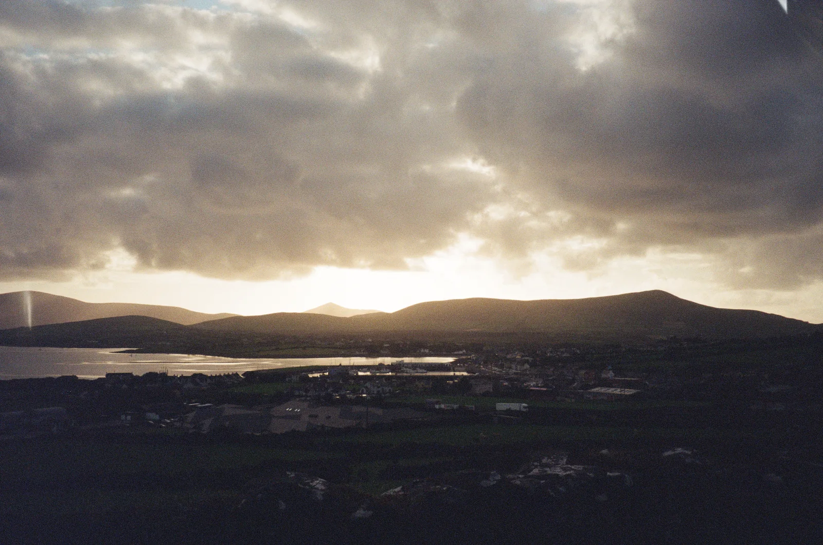 Sunlight breaking through clouds above dark rounded hills