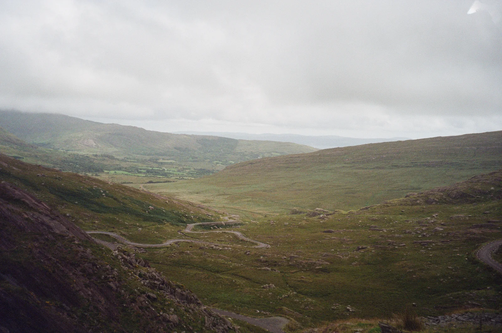 A narrow road winding through a broad green highland valley