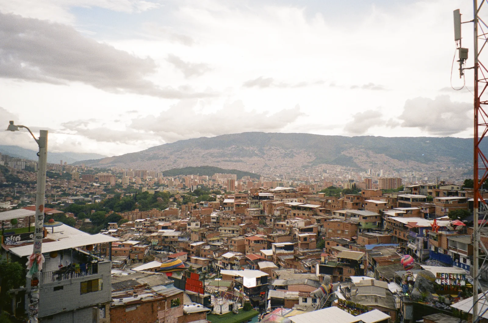 A hillside city spread beneath mountains and broken clouds